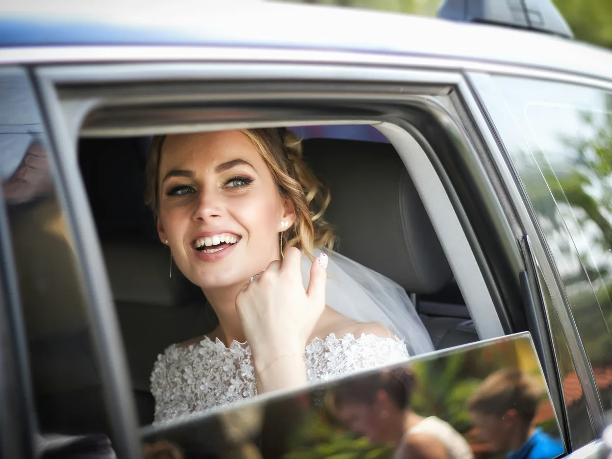 Smiling bride in her wedding dress looking out the window of a car